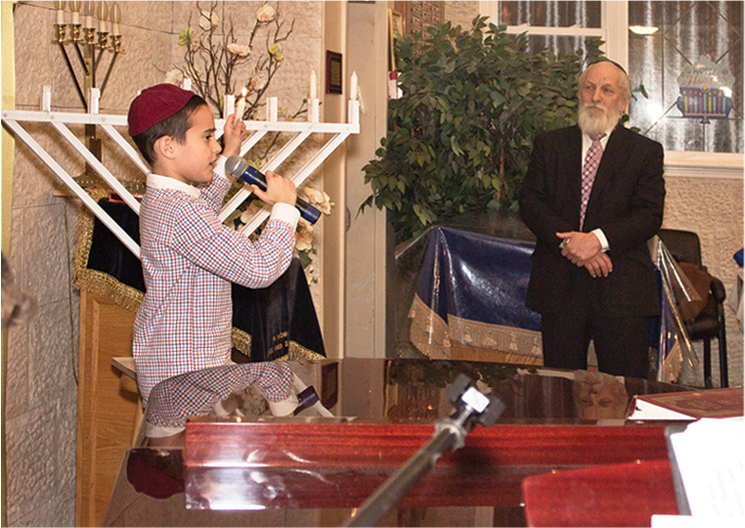 Boy lighting a Chanukah menorah alongside Rabbi Sirota